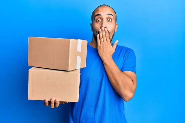 Hispanic Adult Man Holding Packages Blue Background Covering Mouth Hand — Stock Photo, Image