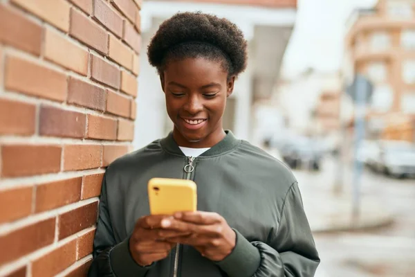 若いアフリカ系アメリカ人の女の子が市内でスマートフォンを使って笑顔で — ストック写真