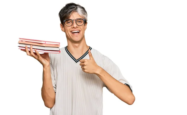 Joven Hombre Hispano Sosteniendo Libros Sonriendo Feliz Positivo Pulgar Hacia —  Fotos de Stock