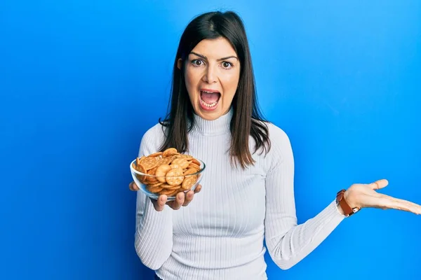 Young Hispanic Woman Holding Salty Biscuits Bowl Celebrating Achievement Happy — Stock Photo, Image