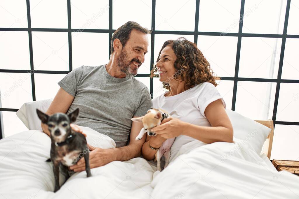 Middle age hispanic couple smiling happy lying on the bed with dogs at home.