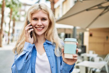 Genç sarışın kadın güneşli bir günde telefonda konuşuyor.