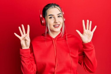 Genç, modern bir kız spor kıyafetleri giyiyor ve kulaklık takıyor. 9 numaralı parmaklarıyla işaret ediyor. Kendinden emin ve mutlu bir şekilde gülümsüyor.. 