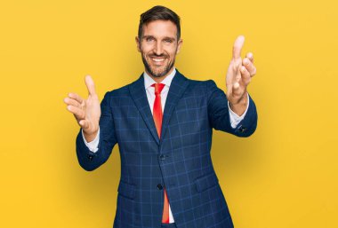 Sakallı, takım elbiseli ve kravatlı yakışıklı. Kameraya bakıp kucaklaşmak için gülümsüyor. Mutluluğu kucaklayan neşeli bir ifade.. 