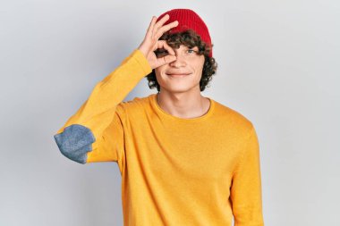 Yün şapka takan yakışıklı genç adam el hareketleriyle gülümsüyor ve mutlu yüzüyle parmaklarının arasından bakıyor.. 