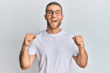 Gündelik giysiler ve gözlük takan genç beyaz adam kollarını kaldırıp, gözlerini açarak başarıyı kutluyor ve şaşırıyor. Kazanan konsept. 
