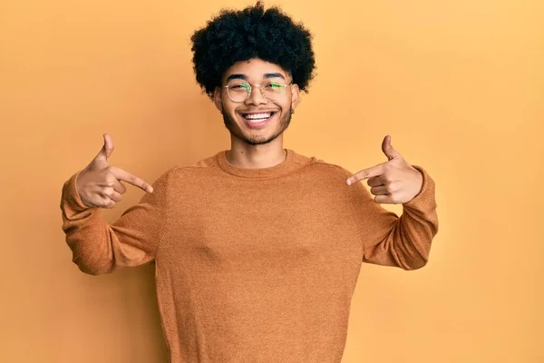 若いですアフリカ系アメリカ人男性とともにアフロヘアを身に着けていますカジュアルな冬のセーターを身に着けています笑顔で自信を持って顔に 指で自分自身を指して誇りと幸せ — ストック写真