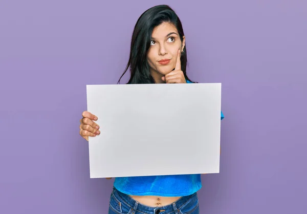 Mujer Hispana Joven Sosteniendo Banner Vacío Blanco Cara Seria Pensando —  Fotos de Stock