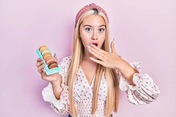 Menina Loira Jovem Segurando Deliciosos Doces Macarons Cobrindo Boca Com — Fotografia de Stock