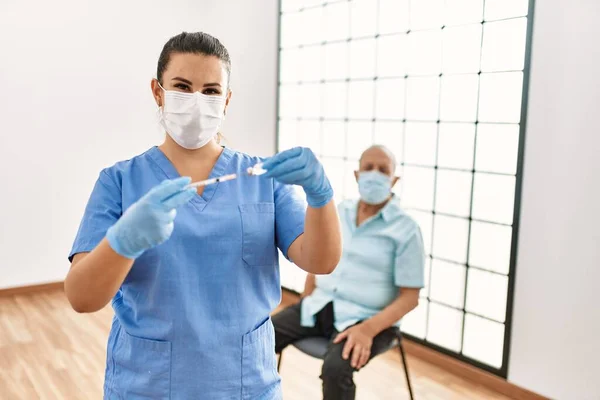 Young nurse wearing safety mask preparing coronavirus vaccine to vaccinate senior man