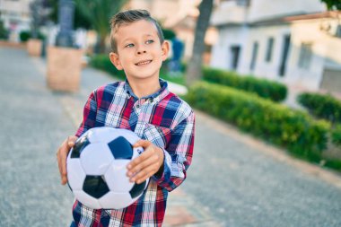 Parkta futbol topunu tutarken mutlu gülümseyen sevimli beyaz çocuk..
