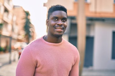 Genç Afrikalı Amerikalı adam gülümseyerek şehirde mutlu mesut duruyor..