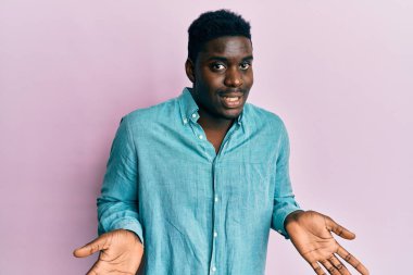 Yakışıklı, sıradan kıyafetler giyen, kafası karışmış, elleri ve kolları havada bir zenci. şüphe kavramı. 