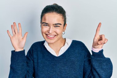 Gündelik giysiler giyen genç beyaz kız altı numarayı gösterip işaret ederken kendinden emin ve mutlu gülümsüyor.. 