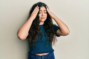 Kıvırcık saçlı genç esmer kadın stres yüzünden elleri başının üstünde günlük kıyafetler giyiyor. migren ağrısı. 