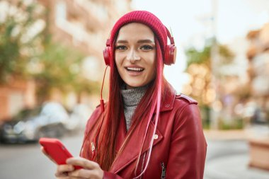 Beyaz kız şehirde akıllı telefon ve kulaklık kullanarak mutlu bir şekilde gülümsüyor..