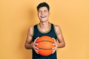 Genç İspanyol adam basketbol topunu tutuyor ve kahkahalarla gülüyor.. 