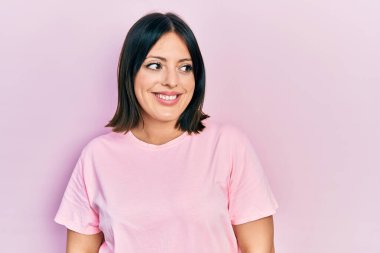 Günlük pembe tişört giyen genç İspanyol kadın yüzünde gülümsemeyle yan yana bakıyor, doğal bir ifade. Kendinden emin gülen. 