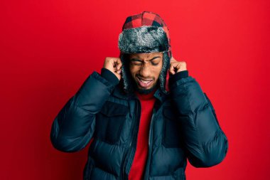 Sakallı, kışlık şapkalı ve paltolu, parmaklarıyla kulaklarını kapatan, gürültülü müzik sesi için rahatsız edici ifadeleri olan genç Afrikalı Amerikalı bir adam. sağır kavramı. 