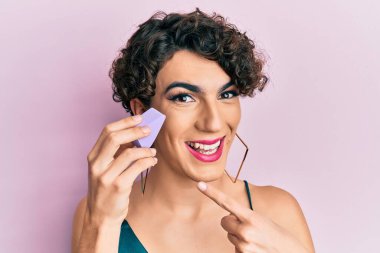 Makyaj süngeri tutan genç adam mutlu bir şekilde el ve parmağıyla işaret ediyor. 