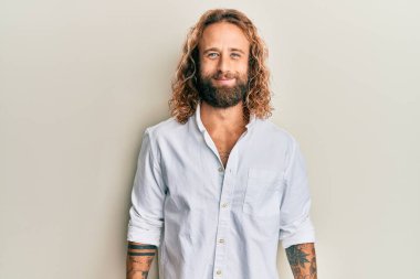 Sakallı, uzun saçlı, sıradan beyaz tişörtlü ve yüzünde güzel bir gülümseme olan yakışıklı bir adam. şanslı kişi. 