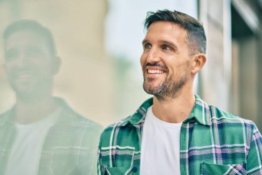 Genç beyaz adam gülümseyerek şehirde mutlu mesut duruyor..