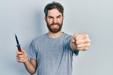 Sakallı, elinde çakı olan beyaz bir adam öfkeyle bağırıyor, öfkeyle bağırıyor ve el kaldırıyor. 