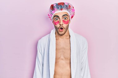 Bornoz ve duş başlığı takan genç İspanyol adam göz torbaları kullanıyor korkmuş ve ağzı açık bir şekilde şaşırmış, inançsız bir yüz. 