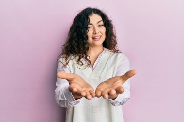 Kıvırcık saçlı, elleri avuçlarında gülümseyen ve el hareketi yapan esmer bir kadın. Bekleme ve koruma 