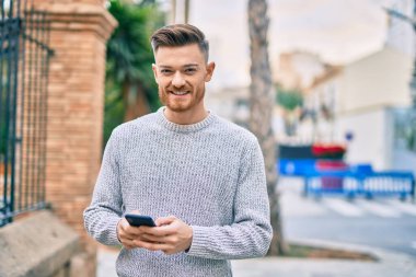 Beyaz adam şehirde akıllı telefon kullanarak mutlu bir şekilde gülümsüyor..