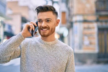 Genç beyaz adam gülümsüyor. Şehirdeki akıllı telefondan konuşuyor..