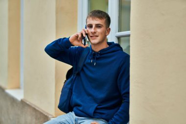 Genç sarışın öğrenci gülümsüyor. Üniversitede akıllı telefondan konuşuyor..