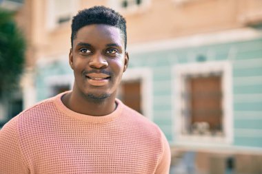 Genç Afrikalı Amerikalı adam gülümseyerek şehirde mutlu mesut duruyor..