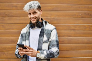 Genç İspanyol adam şehirde akıllı telefon ve kulaklık kullanarak mutlu gülümsüyor..