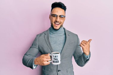 Genç Arap adam, ben patron kahve fincanından içerken baş parmağını yana kaldırıyor ve mutlu bir şekilde gülümsüyor. 