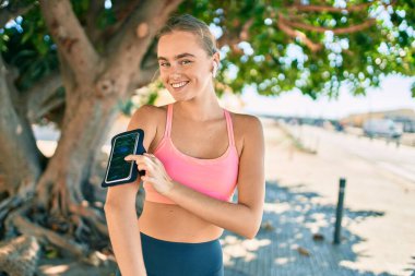 Genç sarışın sporcu, şehirde egzersiz yaparken kulaklık takıyor.