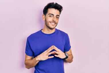 Latin asıllı genç adam rahat ve neşeli bir şekilde ellerini ve parmaklarını çaprazlayarak gülümsedi. Başarı ve iyimserlik 