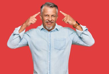 Orta yaşlı, gri saçlı, günlük kıyafetler giyen, iki eliyle başını gösteren, harika bir fikir ya da düşünce, iyi bir hafıza. 