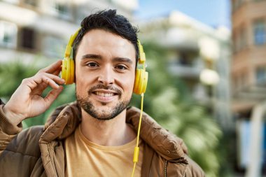 Şehirde kulaklık takarak mutlu gülümseyen genç İspanyol adam..