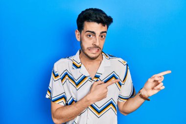 Gündelik kıyafetler giyen genç İspanyol bir adam iki eliyle endişeli ve endişeli bir ifadeye işaret ediyor. 