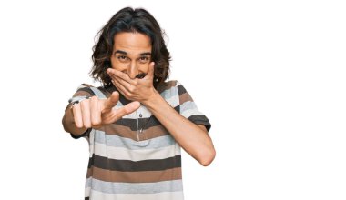 Gündelik kıyafetler giyen genç İspanyol adam sana gülüyor, eli ağzında kamerayı işaret ediyor, yüz ifadesi utanç verici. 