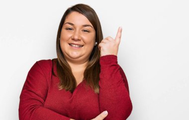 Güzel esmer, iri yarı, günlük kıyafetler giyen, yüzünde kocaman bir gülümseme olan, eli ve parmağı kameraya bakan bir kadın.. 