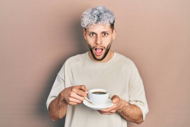 Modern boyalı saçlarıyla bir fincan kahve içen genç İspanyol adam şaşkınlık ve şaşkınlık dolu bir ifade, korku ve heyecanlı bir yüz ifadesiyle şok olmuştu.. 