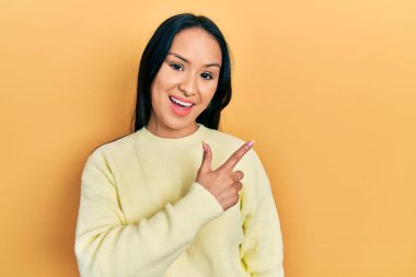 Güzel İspanyol bir kadın, burun piercing 'i takıyor, sarı bir süveter giyiyor, gülümsüyor, eli ve parmağı yana doğru uzanıyor. 