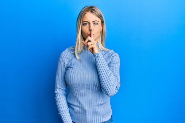 Güzel sarışın kadın gündelik kıyafetler giyip parmakları dudaklarında sessiz olmak istiyor. sessizlik ve gizli konsept. 