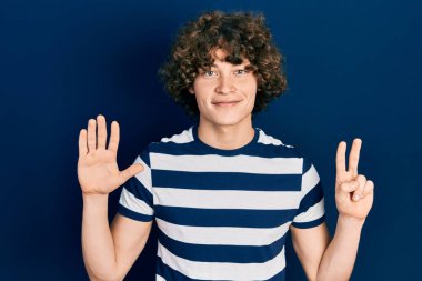 Yakışıklı, çizgili tişört giymiş yedi numaralı parmaklarıyla onu gösterirken kendinden emin ve mutlu bir şekilde gülümsüyor.. 