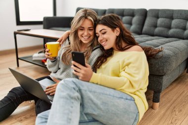 Laptop ve akıllı telefon kullanan genç bir çift evde kahve içiyor..