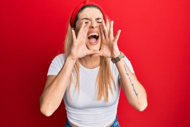 Beyaz gündelik tişört giyen genç beyaz kadın elleri ağızda bağırarak bağırıyor. 