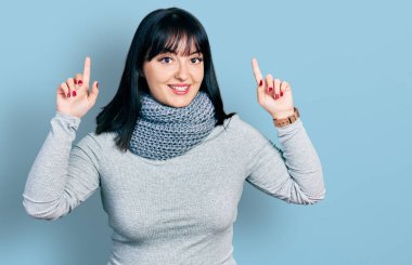 Kış eşarbı takan Latin kökenli genç bir kadın. Şaşırmış, şaşırmış ve parmaklarıyla işaret ediyor ve kollarını kaldırıyordu.. 