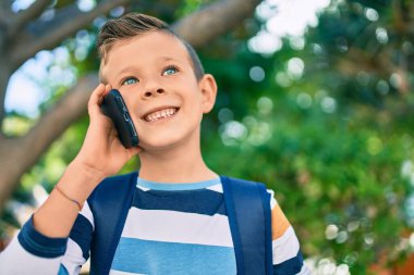 Sevimli beyaz çocuk gülümsüyor. Parktaki akıllı telefondan konuşuyor..